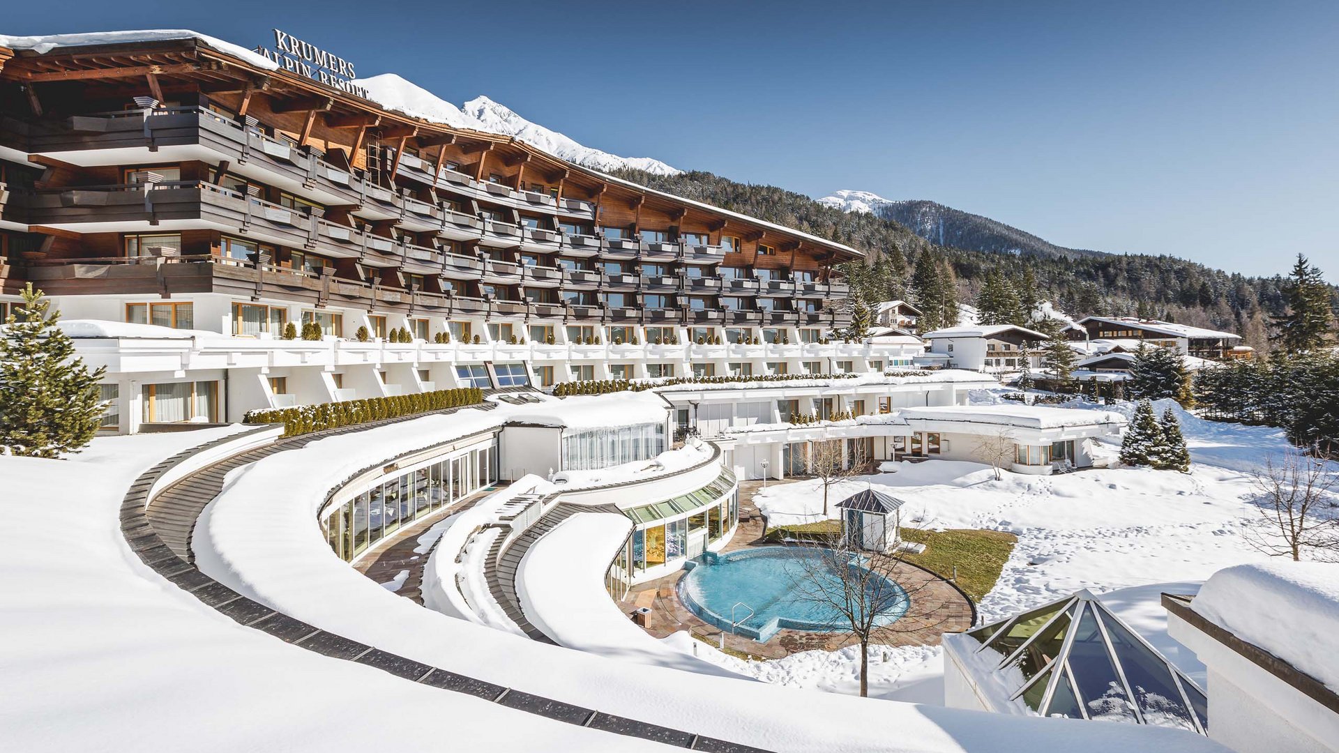Erfrischung im Hotel in Seefeld mit Pool Hotel mit Schnee bedeckt, Alpenlandschaft und Außenpool unter klarem Himmel