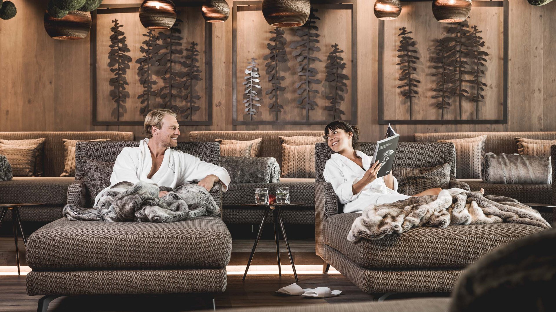 Day Spa in Seefeld Paar entspannt in Bademänteln auf Sesseln mit Decken in gemütlicher Lounge