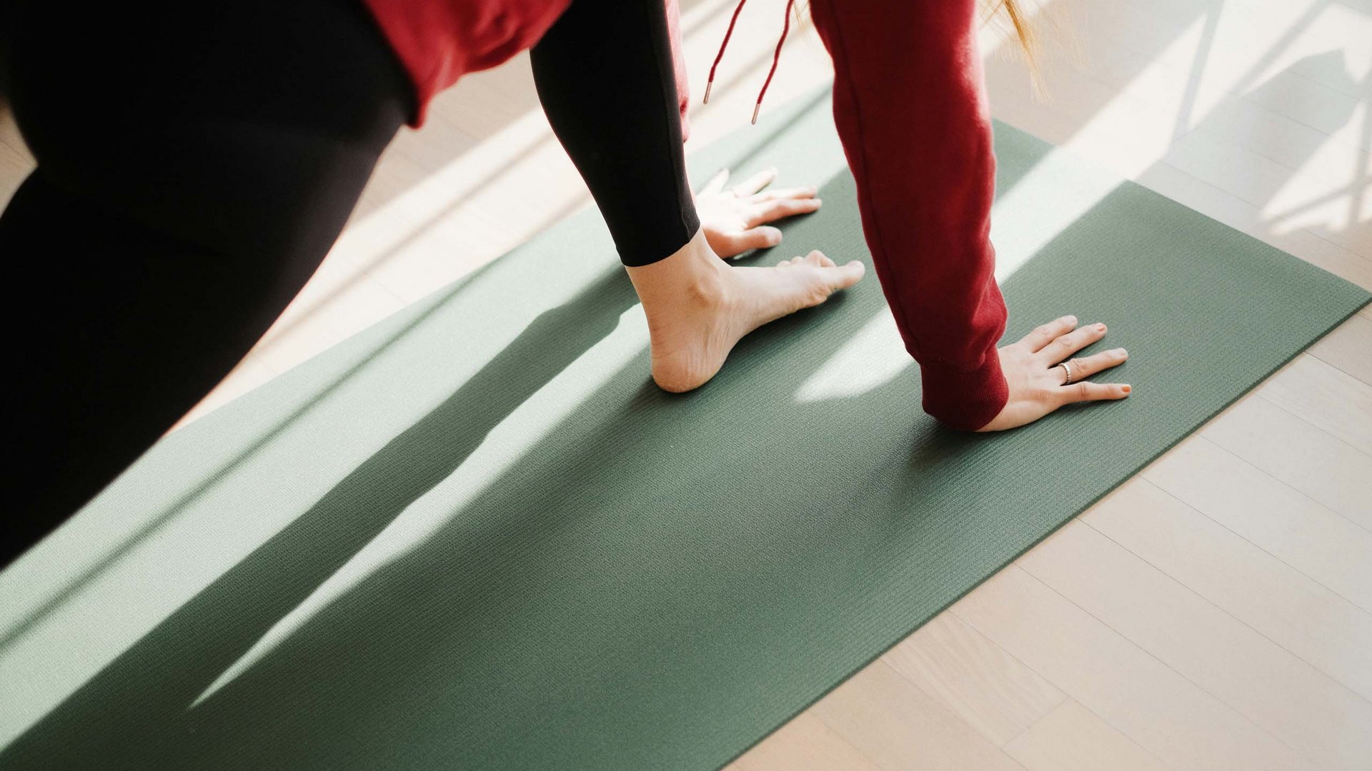 Ihr Yogahotel in Tirol Person macht Yoga Dehnung auf grüner Matte im Sonnenlicht