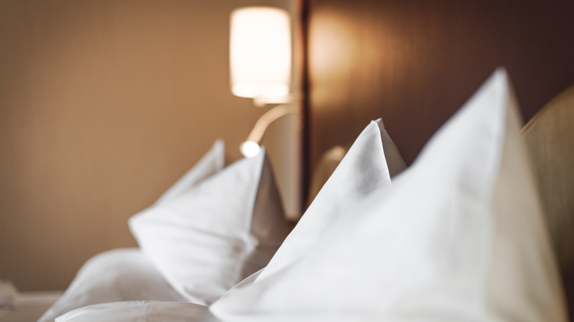 Ihr Zimmer in Seefeld in Tirol Nahaufnahme von weißen Kissen auf einem Bett mit Wandlampe im Hintergrund